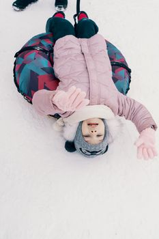 little girl in a knitted hat and scarf and an inflatable sled.