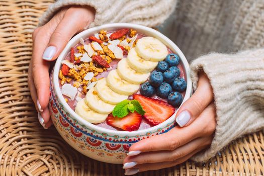 Woman hands holding fresh fruit acai smoothie bowl. Healthy vegan smoothie bowl with banana, strawberry, blueberry and granola. High quality photo