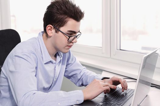 Attractive teenage boy with glasses using his laptop