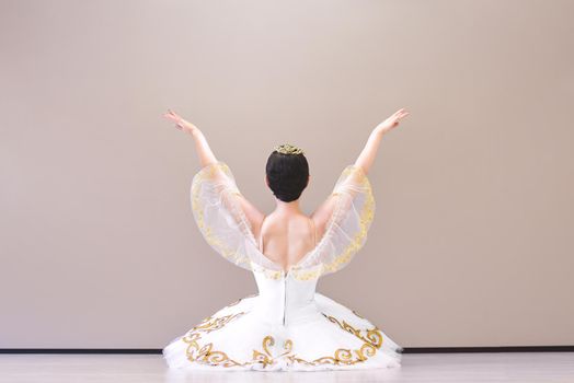 Portrait from back view of a charming ballerina is sitting on the floor in the ballroom warming up before the performance