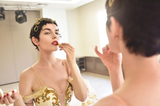 Happy Morning. An attractive young woman ballerina looks at herself in the mirror and put lipstick on her lips.