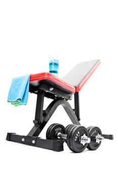 Iron dumbbells beneath a workout bench, blue towel, and water bottle, isolated on white background. Home and gym workout accessories. Sprot and health care concept.

