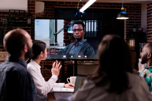 Selective focus on tv screen with serious looking african american business owner in online video conference at office. Team in late night meeting working overtime greeting ceo in internet call.