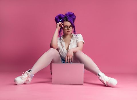 the sexy girl with glasses and purple hair with a laptop on a pink background