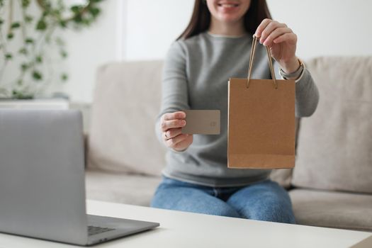 Young woman holding credit card and using laptop at home. Paying online, home shopping, internet banking, electronic store concept.