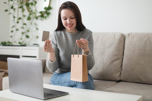 Young woman holding credit card and using laptop at home. Paying online, home shopping, internet banking, electronic store concept.