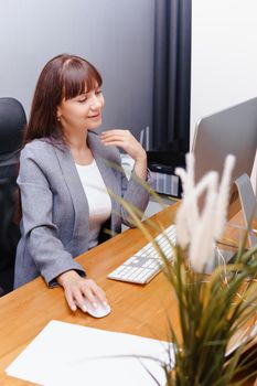 A brunette woman at a computer in the workplace. Business concept.