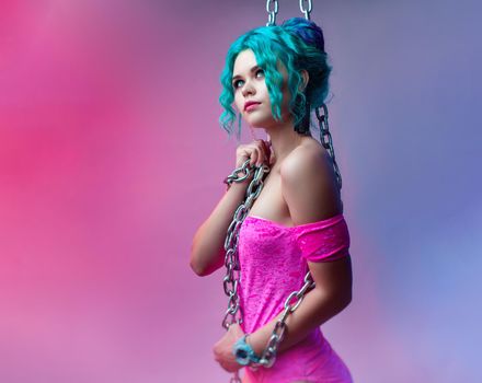 the sexy girl with colored hair in a bright pink bodysuit with a metal chain on a neon background