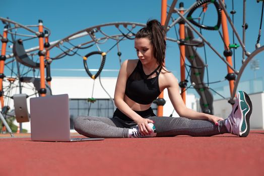 sporty girl does fitness on a sports field in the summer outdoors with a laptop