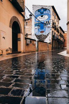 A graffiti on a facade and reflected on the floor in a street of Huesca