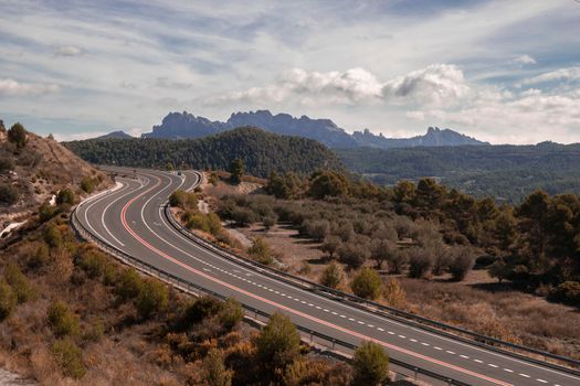 Curved road and Montserrat mountain in the background in a landscape under a cloudy sky in Catalonia