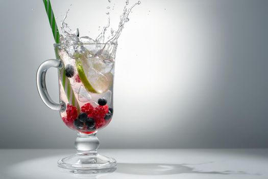 Refreshing summer cocktail with ice, lime and berries in a glass with a straw, copyspace.