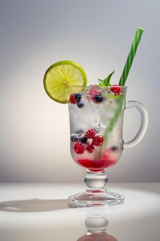 Refreshing summer cocktail with ice, lime and berries in a glass with a straw, vertical image.