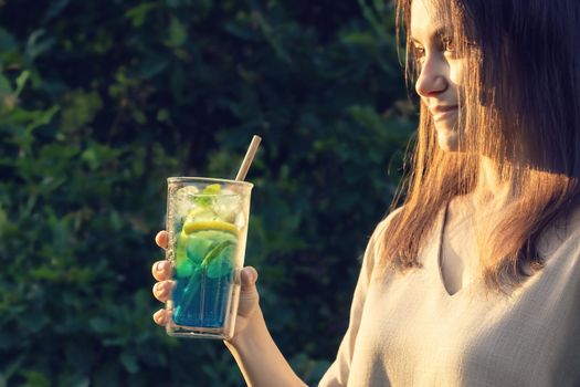 Young woman with long dark hair holds a summer refreshing cocktail in her hand. Selective focus.