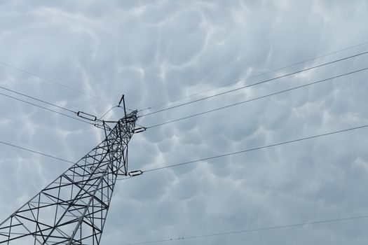 A tall power pole seen from below against a background of storm clouds in the shape of bubbles compressed one next to the other.