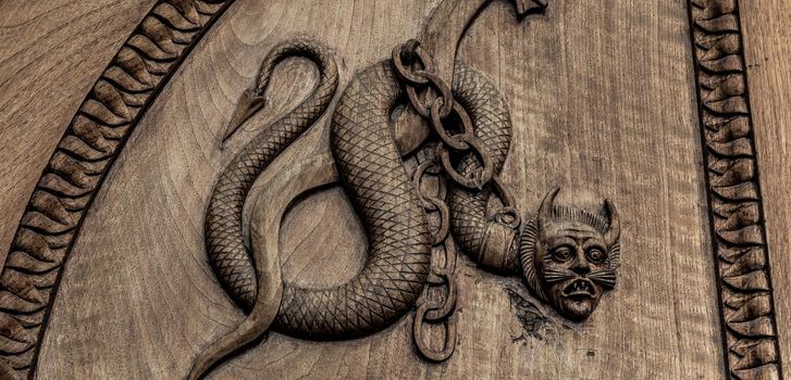 Devil snake symbol. Fantasy magic creature on an old door, 12th Century Abbey, Italy.