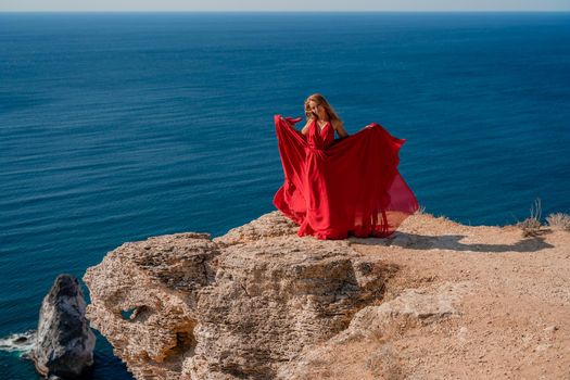 A woman in a red flying dress fluttering in the wind, against the backdrop of the sea