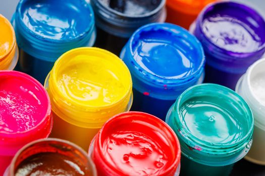 full-frame close-up background of opened small gouache paint jars on black