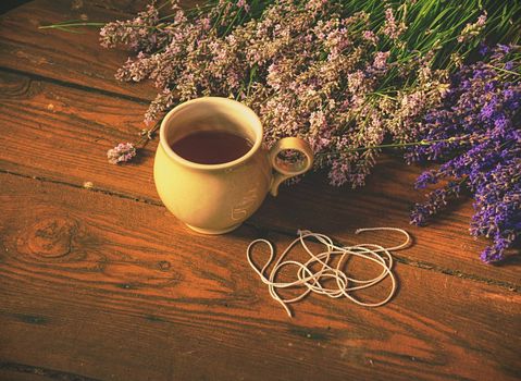 Aroma designer  workplace. Girl prepar harvested lavander stalks for drying. Rustic wooden tble with cup of herbal tea