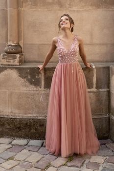 Beautiful brunette bridesmaid with luxury hairdo in gorgeous elegant stylish pale pink chiffon gown dress on flowers background. Wedding day in old beautiful European city.