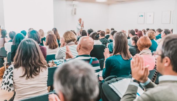 Life coaching symposium. Female speaker giving interactive motivational speech at entrepreneurship workshop. Audience in conference hall. Rear view of unrecognized participant.