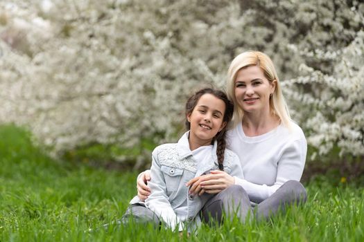 Outdoor portrait of happy young family playing in spring park under blooming tree, lovely family having fun in sunny garden.