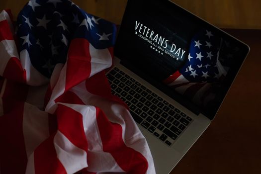veterans day written in laptop with flag of the United States, on a rustic wooden background.