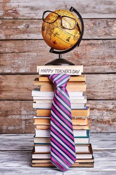 Glasses on globe and tie. Stack of books and card. Congratulate geography teacher.