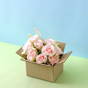 Flowers pink roses in a cardboard delivery box on a pastel background as an idea for delivery and congratulations and a gift.