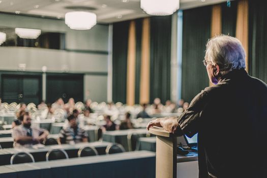 Casualy dressed senior professor giving talk at scientific conference. Audience at the conference hall. Research experts and entrepreneurship event.