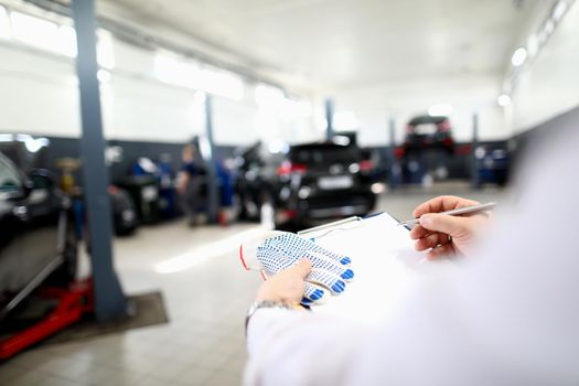 Close-up of male worker writing machine diagnostic data in garage. Fixed car after maintenance in service. Pit stop, service station and handyman concept