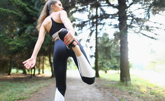 Low angle of fit woman standing back and stretching legs for productive morning run. Sportswoman do every day ritual. Active lifestyle, fitness concept