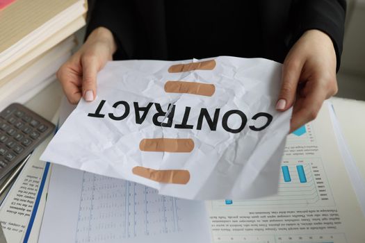 Close-up of torn sheet of paper with word contract glued with adhesive tape. Manager hands holding band-aid paper contract. Recovery contract agreement concept