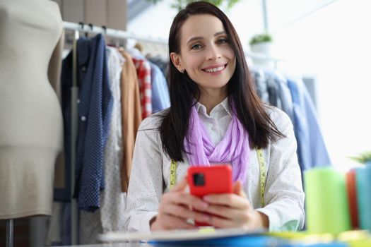 Portrait of female seamstress smiling and posing in sewing workshop. Cheerful female looking at camera with happiness. Designer, art and sewing concept