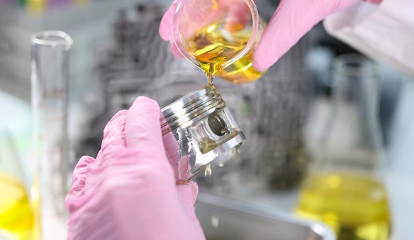 Close-up of person hand in gloves holding piston and pours lubricating oil on it. Mechanic fix car details. Lab, pit stop and service station concept