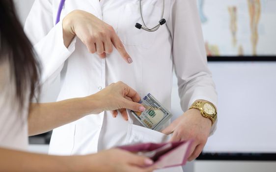 Close-up of female hand putting money to doctor pocket. Patient paying medical service. Bribe to practitioner. Corruption in medicine