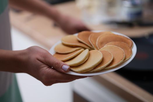 Close-up of female hands holding plate with tasty fresh homemade pancakes. Hot delicious meal for breakfast, nutritious food to start day. Food, eating concept