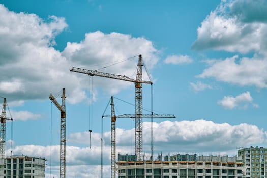 Industrial building cranes on background of cloudy sky. Construction site background with copy space. Hoisting cranes for creating multi-storey buildings of new city districts.