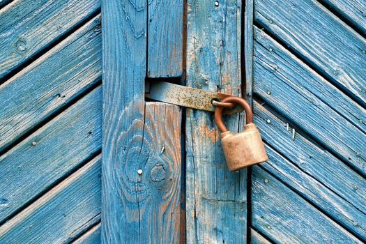 Closeup of old padlock on a weathered retro blue wooden door.