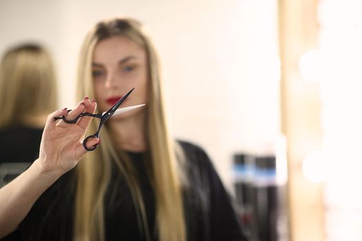 Portrait of female hairdresser holding scissors in hand, master ready to change client image. Beauty studio, self care and wellness concept