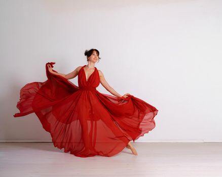 Dancer in a red flying dress. Woman ballerina dancing on a white studio background.