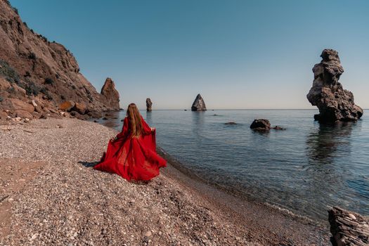 Beautiful sensual woman in a flying red dress and with long hair, stands on the seashore.