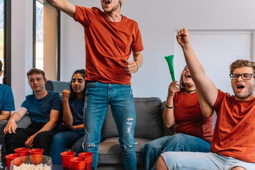 friends jumping for joy after their team's victory, watching football match on TV. opposing team sad after defeat leisure concept, three young adults in blue t-shirts. happy and cheerful. natural light in the living room at home.