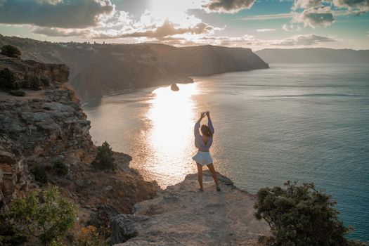 Free girl with open arms at sunset over the sea, sun over clouds, sunset in the mountains, golden hour, silhouette of a woman at sunset on the mountain.