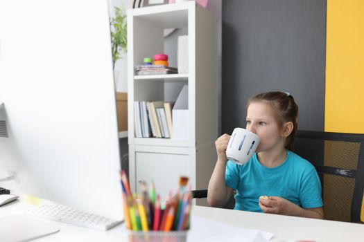 Portrait of little girl using laptop watch funny cartoons at home. Child drinking tea and eating cake. Home entertainment concept
