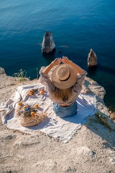 Street photo of a beautiful woman with dark hair in a white top, shorts and a hat having a picnic on a hill overlooking the sea.