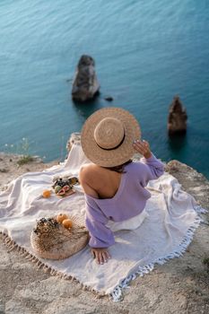 Street photo of a beautiful woman with dark hair in white shorts and a purple sweater having a picnic on a hill overlooking the sea.