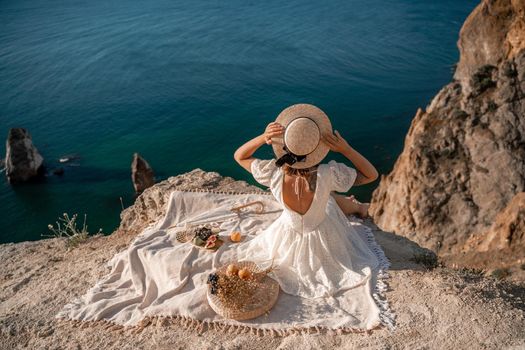 Street photo of a beautiful woman with dark hair in a white dress and hat having a picnic on a hill overlooking the sea.