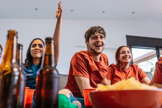 friends hugging after the victory of their sports team broadcast on television. group of young people partying at home. concept leisure concept. happy and cheerful. natural light in the living room at home. trumpet