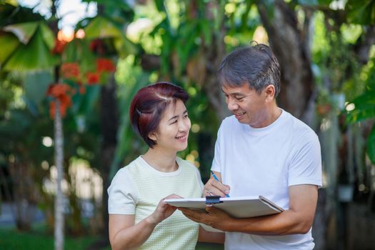 Asian middle-aged couple talking and designing garden plan together in backyard.